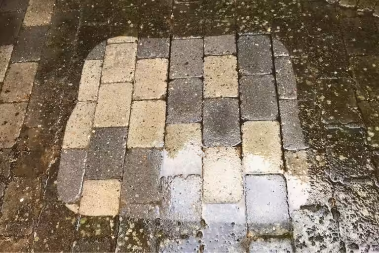 Bild av ett markstensparti där Nanostone visar skillnad mellan nyligen rengjorda, våta betong- och gatstenar och omgivande mörka, mossbelagda ytor; tydliga rengöringsspår och vattenpölar syns på rektangulära stenar. Dokumentation av altantvätt, stentvätt och takbehandling med tydlig före- och efterkontrast.